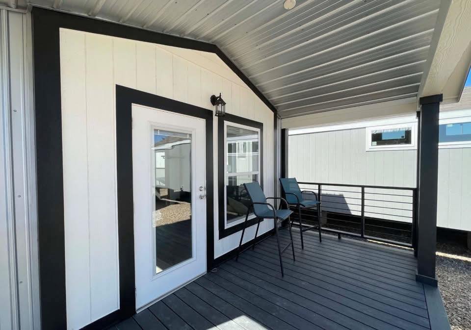 Covered porch with a modern design, featuring black and white trim, a glass door, a small table set, and a metal railing, conveying a calm, inviting atmosphere.