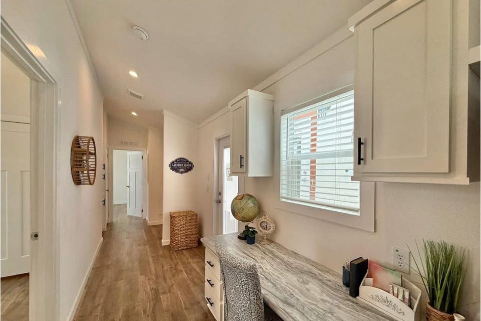 Bright hallway with wood flooring, white walls, and a window on the right. A desk with a globe is underneath, and a wicker basket is near the door. Cozy and inviting.