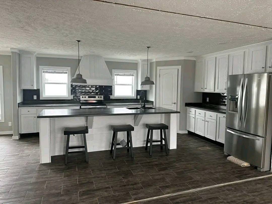 Spacious modern kitchen with dark wood flooring, white cabinets, and stainless steel appliances. Features a large island, bar stools, and pendant lights.