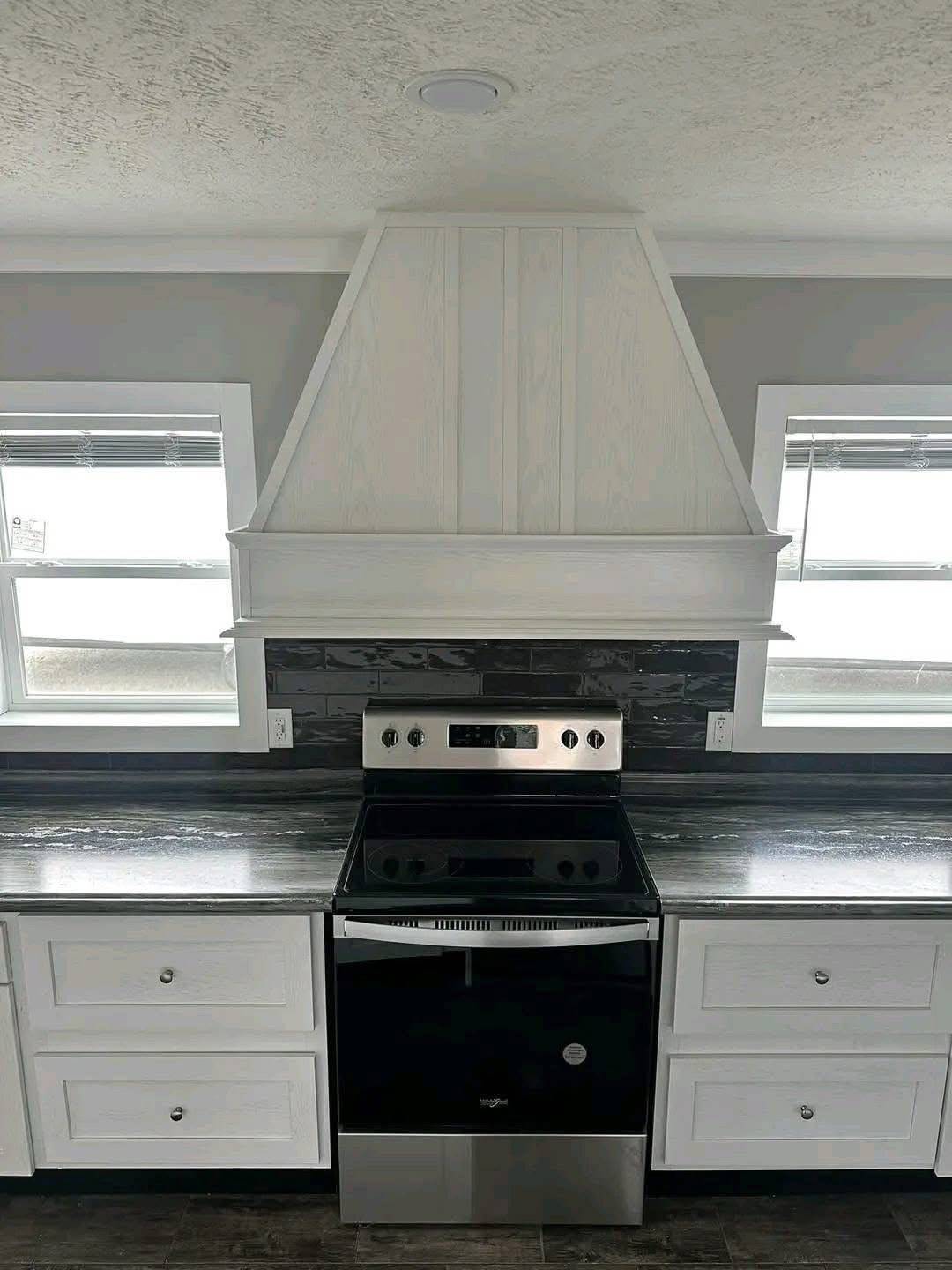 Modern kitchen with stainless steel stove, black backsplash, and gray countertops. White cabinetry and hood add a clean, minimalist aesthetic.