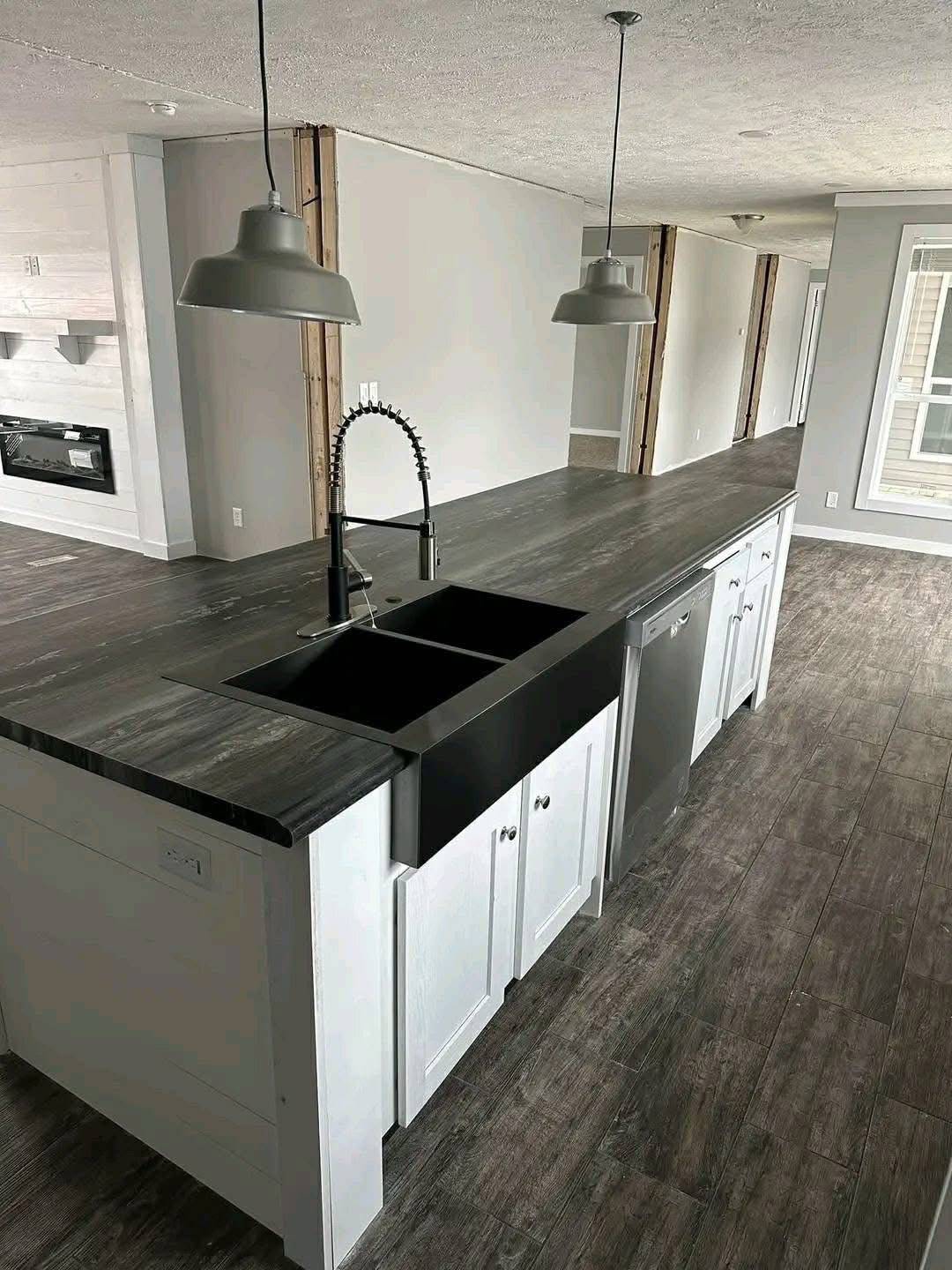 Modern kitchen interior with a long, dark countertop featuring a sleek black sink, white cabinets, pendant lights, and dark wood flooring.