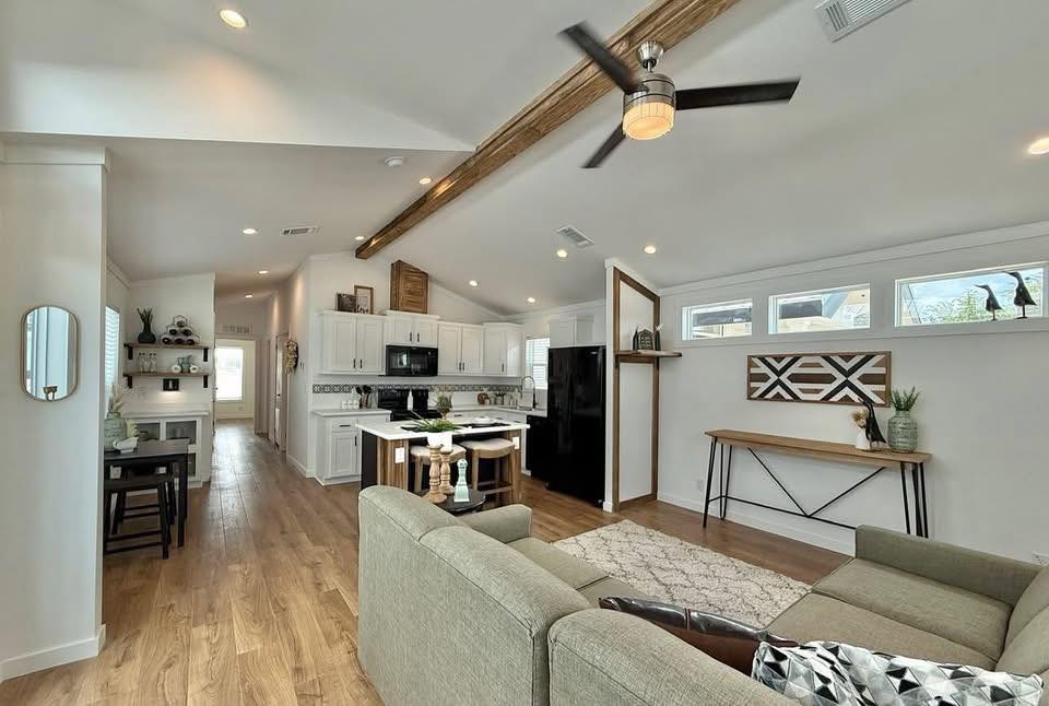 Modern living space with light wood floors and vaulted ceiling. Features a kitchen with white cabinets, an island and sleek decor, creating an airy, open feel.