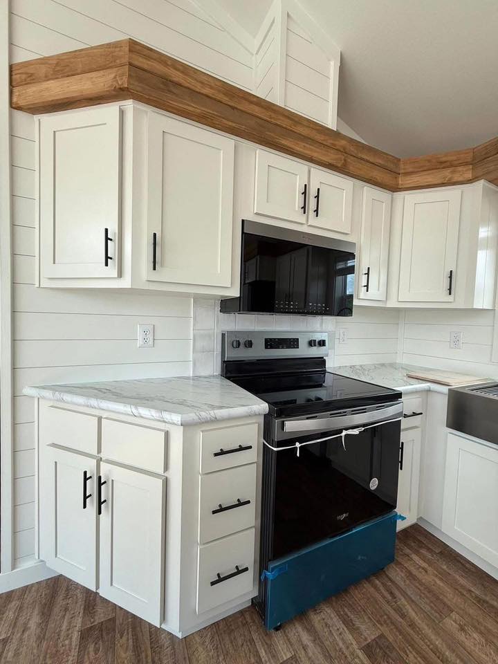 Modern kitchen with white cabinets and black handles. Features a stainless steel oven and dark microwave, wood trim, and marble countertops.