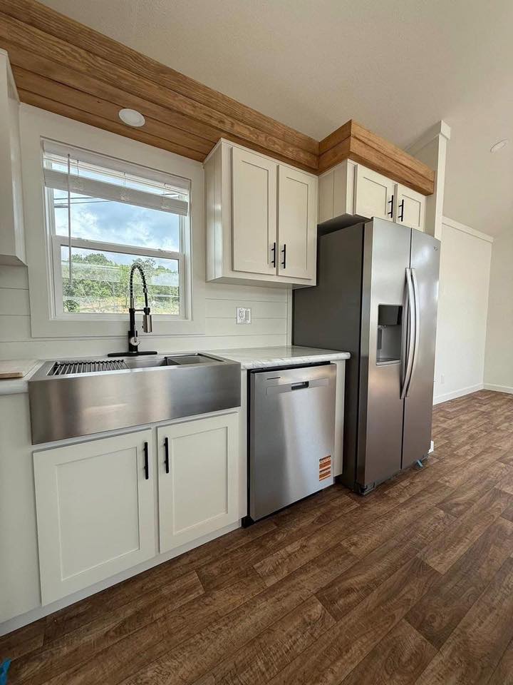 Modern kitchen with stainless steel appliances, including a fridge, dishwasher, and farmhouse sink. White cabinets and wood accents add warmth.