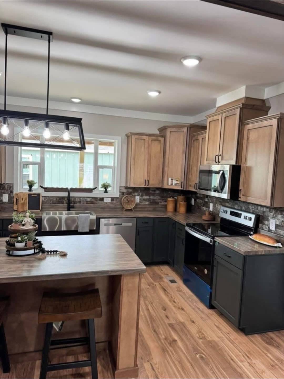 Modern kitchen with light wood cabinets, dark lower drawers, and stainless steel appliances. Features a central island with bar stool and a stylish light fixture above, creating a cozy, inviting atmosphere.