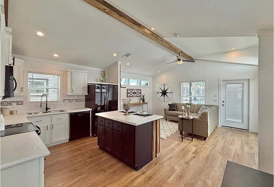 Open-concept kitchen and living room with wooden floors. Features include a central island, modern appliances, cozy seating area, and decorative accents.