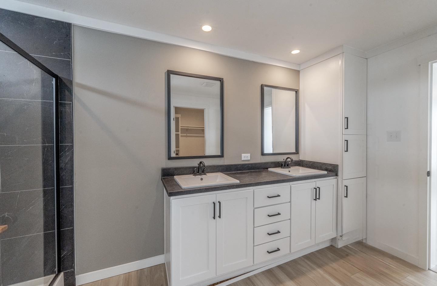 Modern bathroom with dual sink vanity. The space features white cabinets, dark countertops, two mirrors, and wood-like tile flooring, creating a clean, elegant look.