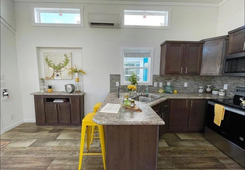 A modern kitchen with dark wood cabinets, marble countertops, and stainless steel appliances. Bright, with yellow stools and cheerful decor.