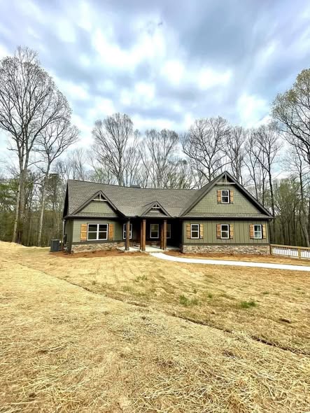 Single-story cabin-style house with green siding and exposed brick foundation, surrounded by bare trees, under an overcast sky, conveying a serene, rustic vibe.
