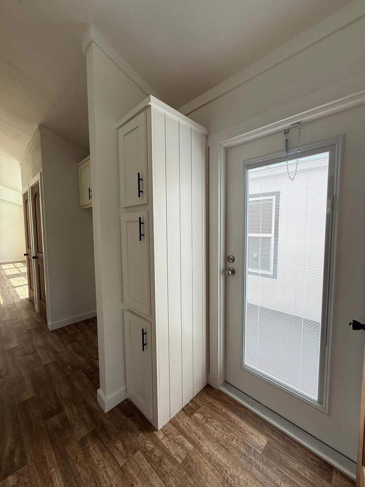 A bright room with a wooden floor features a white door with built-in blinds, next to vertical cabinets with black handles. The atmosphere is modern and minimalistic.