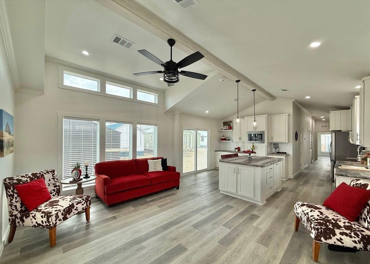 Spacious living room with vaulted ceiling, featuring a red sofa, cowhide-patterned chairs, and a modern kitchen island. Bright, airy, and inviting.