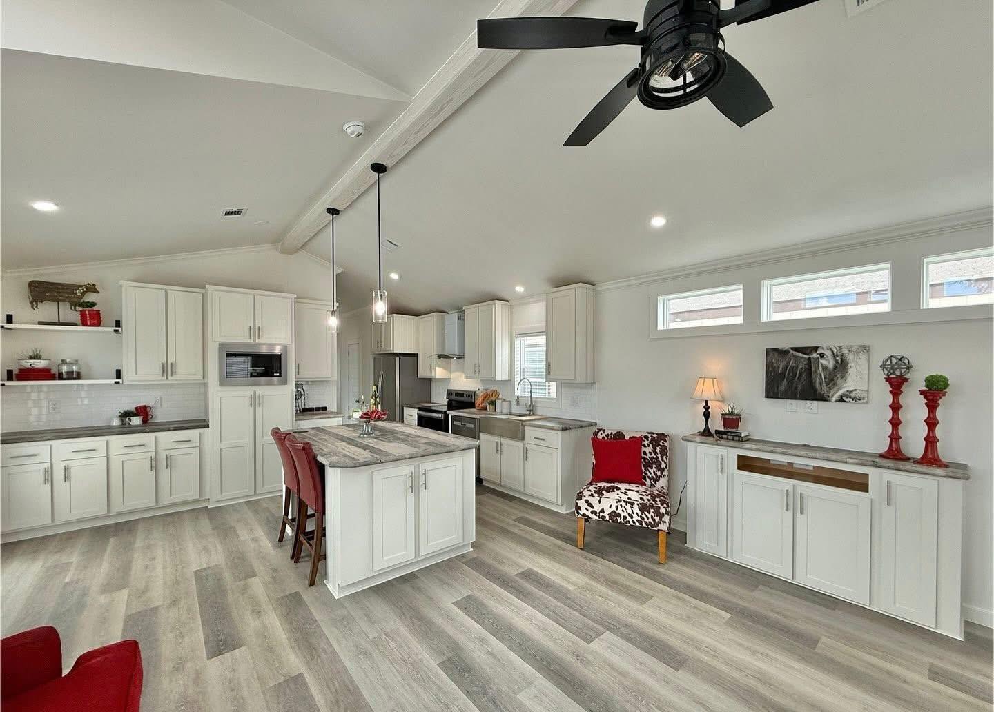 Bright, modern kitchen with white cabinets, gray flooring, and a central island with red chairs. Stylish decor includes red accents and pendant lighting.