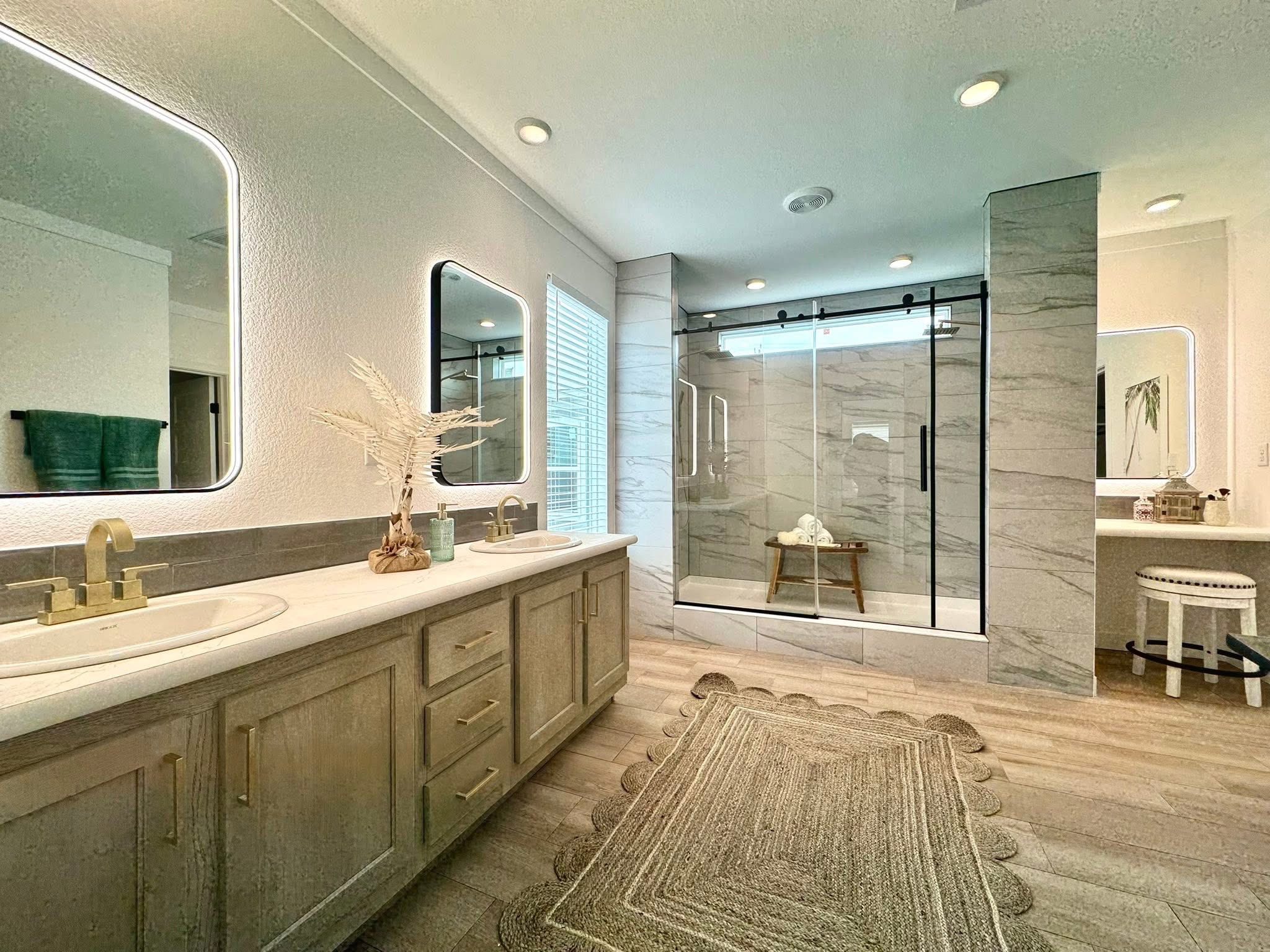 Spacious bathroom with dual sinks on a wooden vanity, frameless mirrors, large glass shower, and modern decor. Warm lighting creates a serene ambiance.
