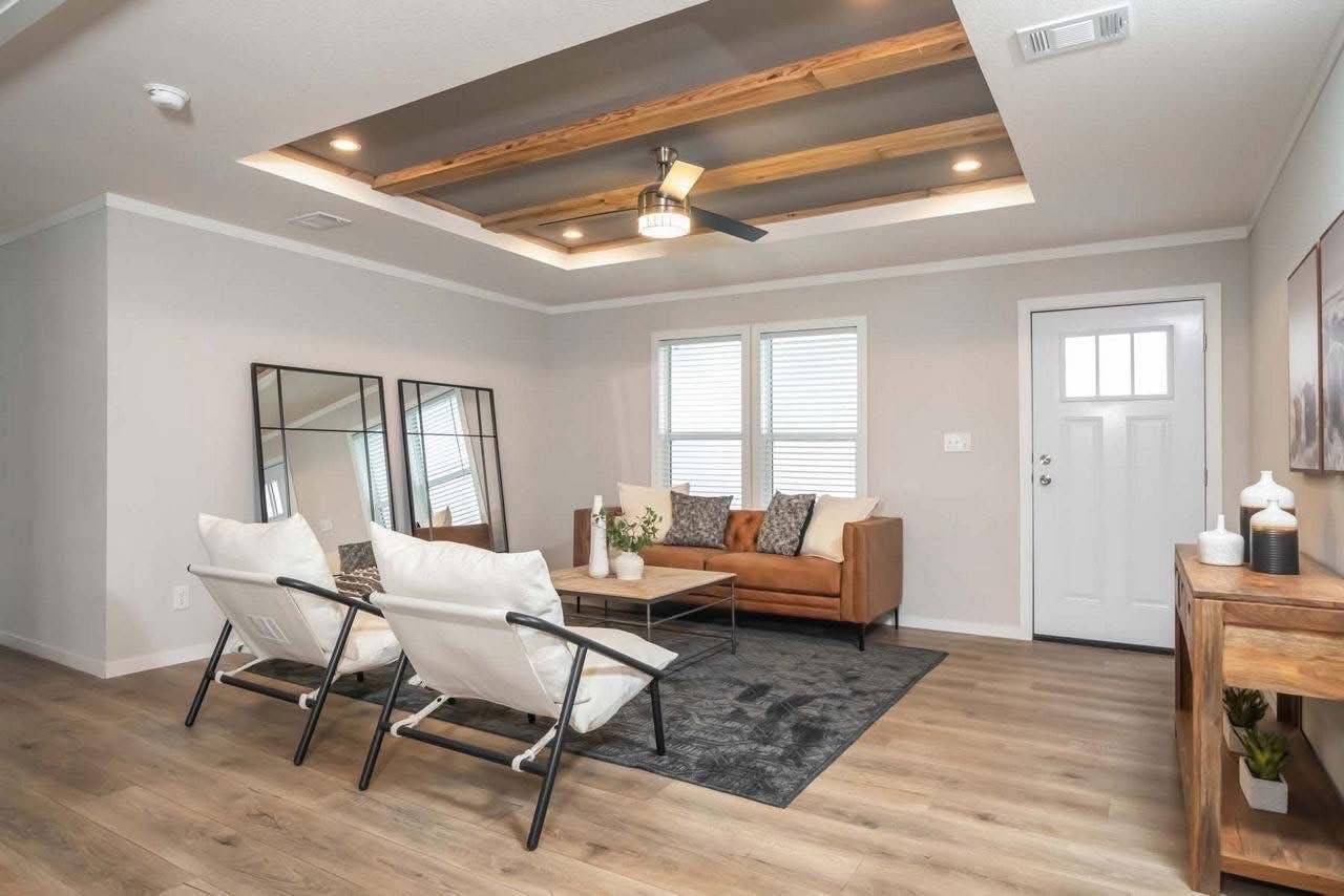 Stylish living room with a modern ceiling fan, brown sofa, and two white chairs. Natural light from dual windows creates an inviting ambiance.