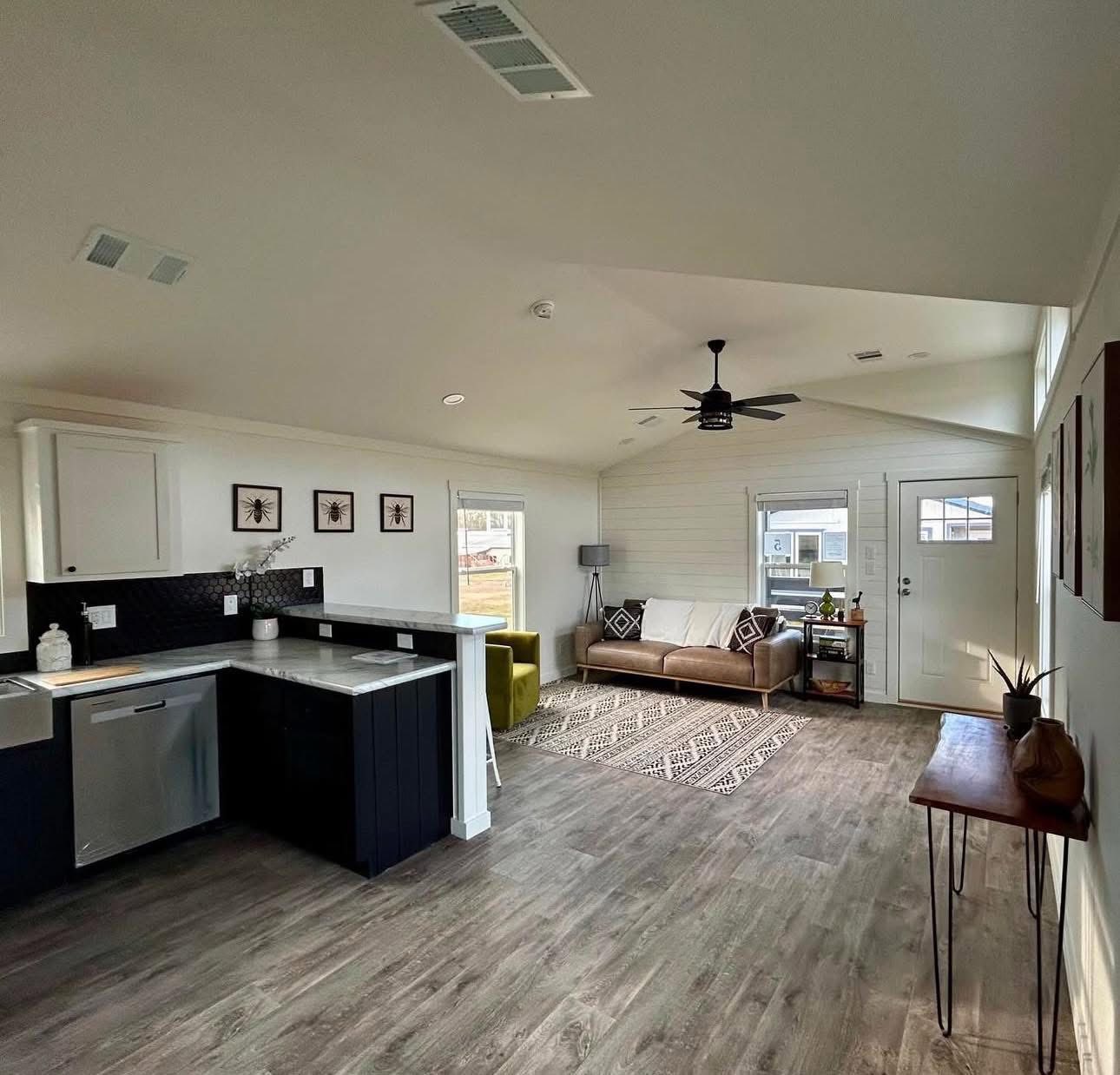 Modern open-concept living area with a brown sofa, patterned rug, and green chair. Nearby, a sleek kitchen features marble countertops. Warm, inviting feel.