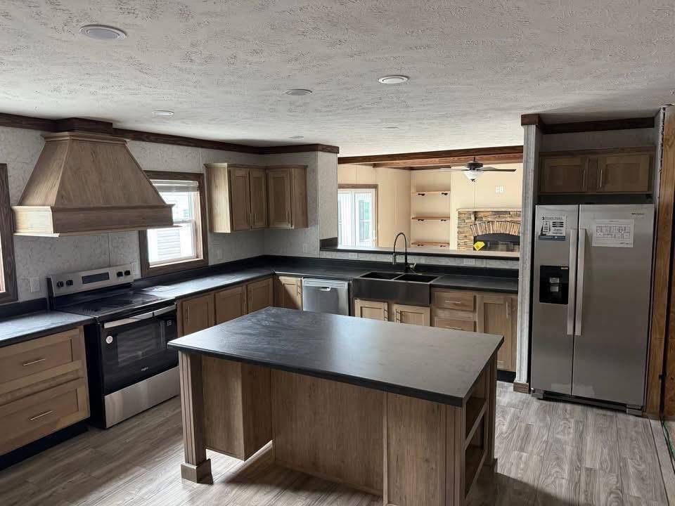Modern kitchen with wood cabinets, black countertops, and an island. Includes stainless steel appliances, a farmhouse sink, and open shelving.