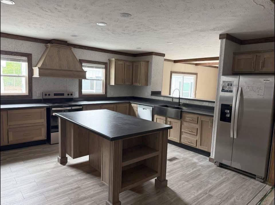 Spacious kitchen with wooden cabinets, a large island, stainless steel appliances, and ample natural light from multiple windows, creating a cozy atmosphere.
