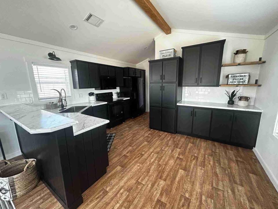 Modern kitchen with dark cabinets, white marble countertops, and wood floors. Open shelves display decor with a cozy, rustic ambiance.