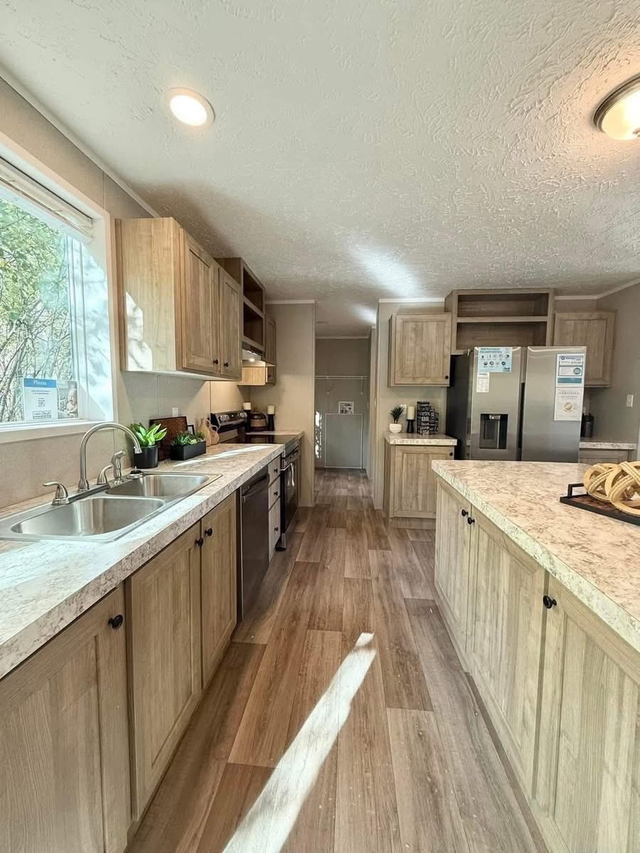 Bright kitchen with wood cabinets, marble countertops, and stainless steel appliances. A window on the left lets in natural light, creating a warm atmosphere.