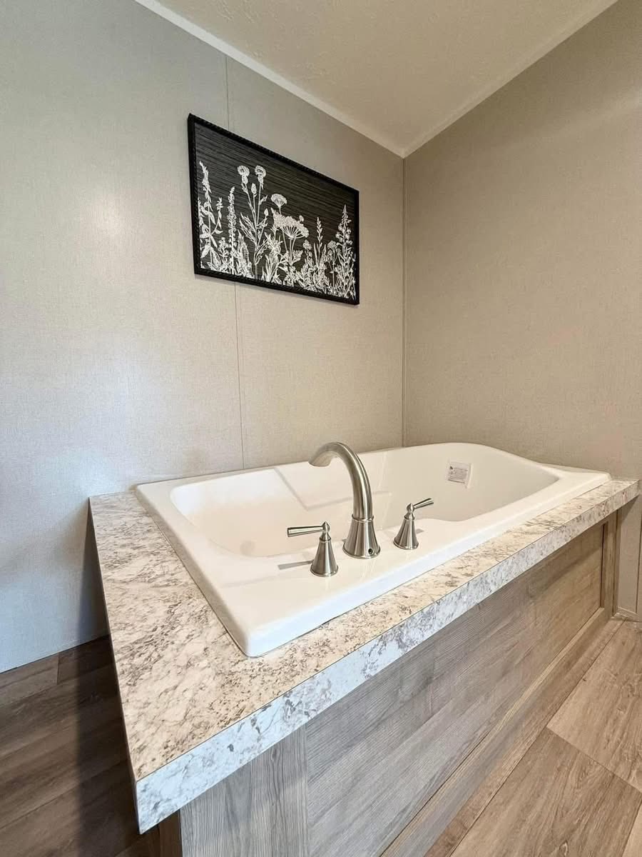 Luxurious bathroom with a marble-topped rectangular bathtub, metallic faucets, and wood paneling. Above, a black and white botanical artwork decorates the wall.