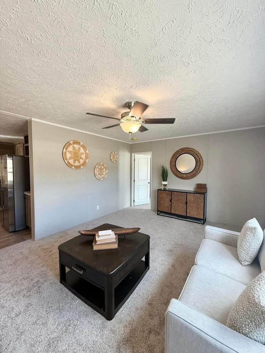 Bright living room with a light beige sofa, decorative pillows, round wall art, wicker console with mirror, and a dark coffee table. Modern and cozy.