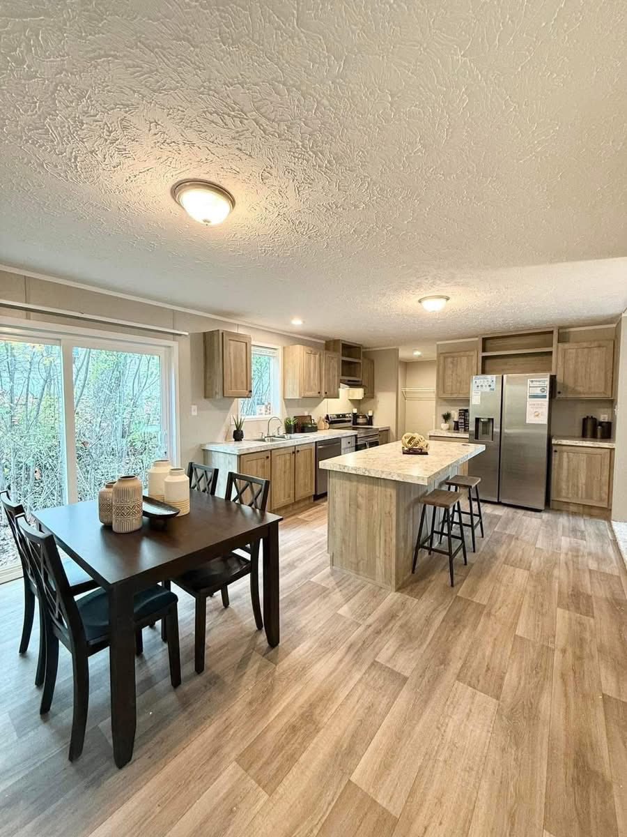 Spacious kitchen with wooden cabinets, a large island with bar stools, and a dining table with decor. Bright, modern, and inviting atmosphere.