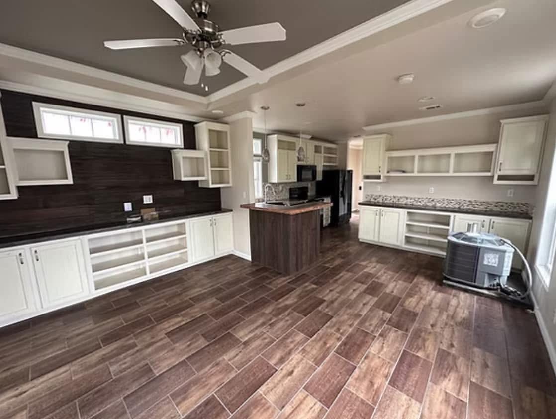 Spacious kitchen with wood flooring, white cabinets, and a dark wood island. Ceiling fan and large windows create a bright, welcoming atmosphere.