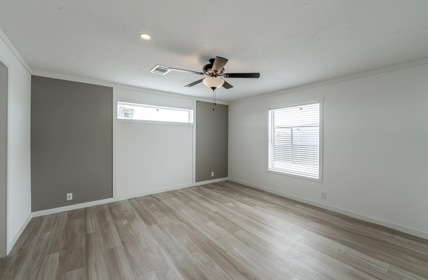 Modern room with light wood flooring, a neutral color palette, a ceiling fan, and large windows. Bright and spacious, conveying a calm ambiance.