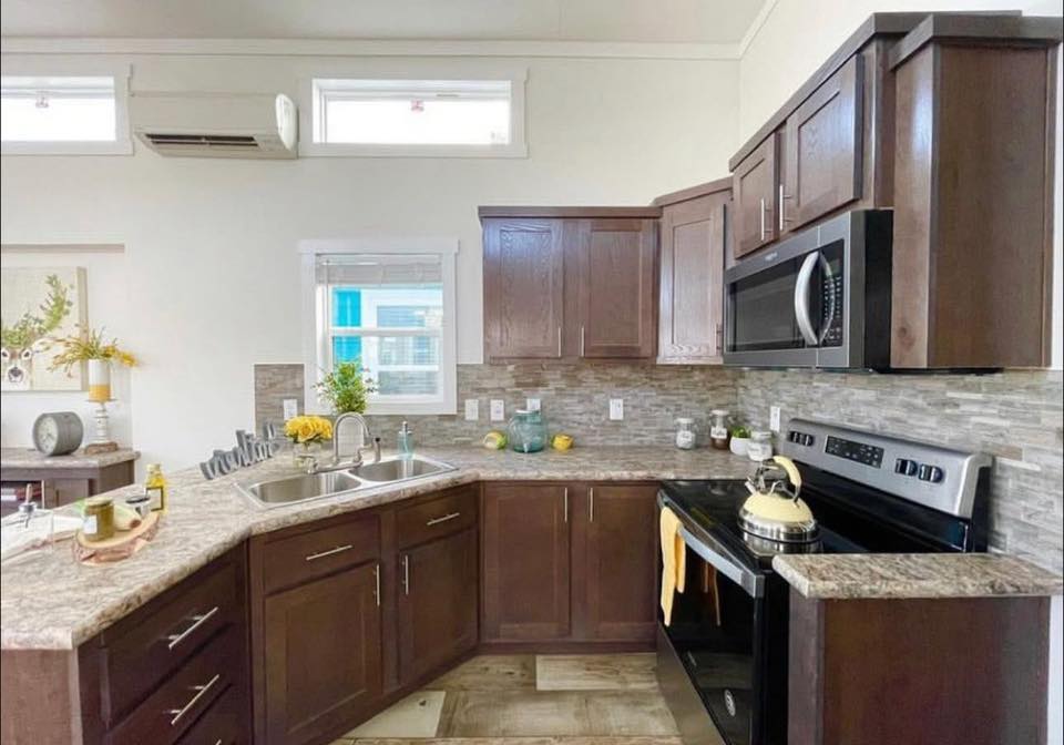 A modern kitchen with dark wood cabinets, granite countertops, and stainless steel appliances. Natural light streams through upper windows, creating a warm, inviting atmosphere.