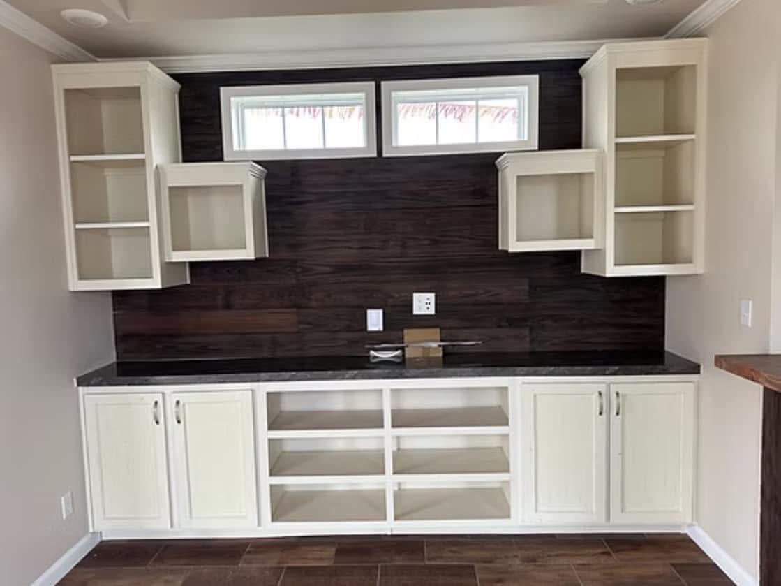Kitchen cabinets with four open white wooden shelves and a dark wood backsplash. Two small upper windows provide natural light. Neutral tone.