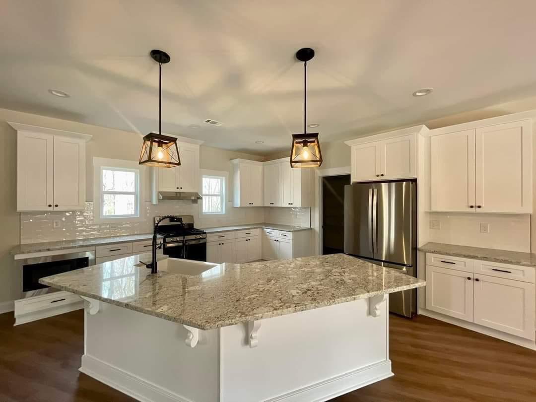 Modern kitchen with white cabinets, granite countertops, and a large island. Two pendant lights hang above, creating a warm, inviting ambiance.