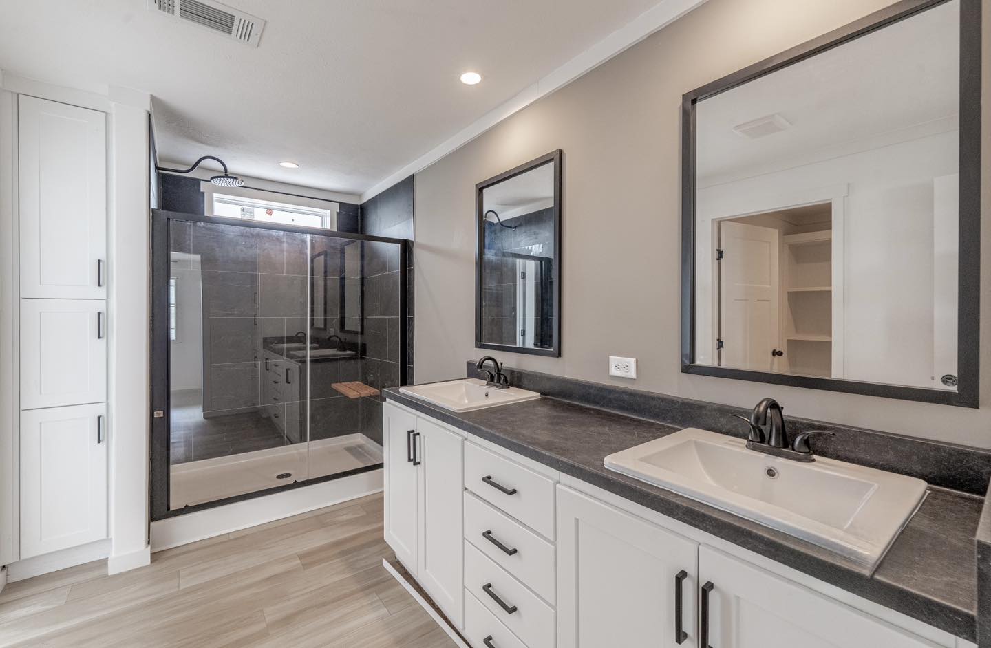 Modern bathroom with a sleek design features a double vanity with two rectangular sinks and black countertops, large mirrors, and a spacious glass shower.