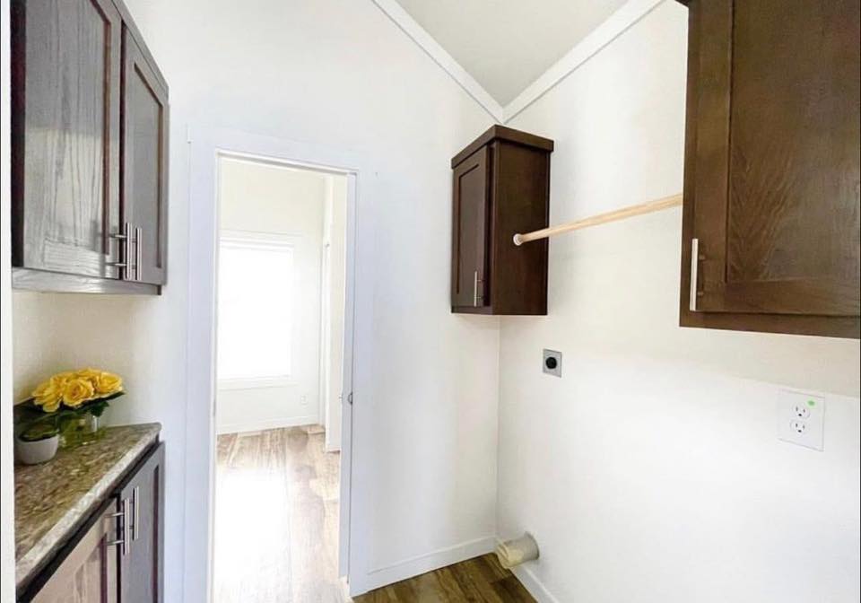 Laundry room with brown cabinets, wooden rod for hanging clothes, and a granite countertop with yellow roses. Bright light from adjacent room.