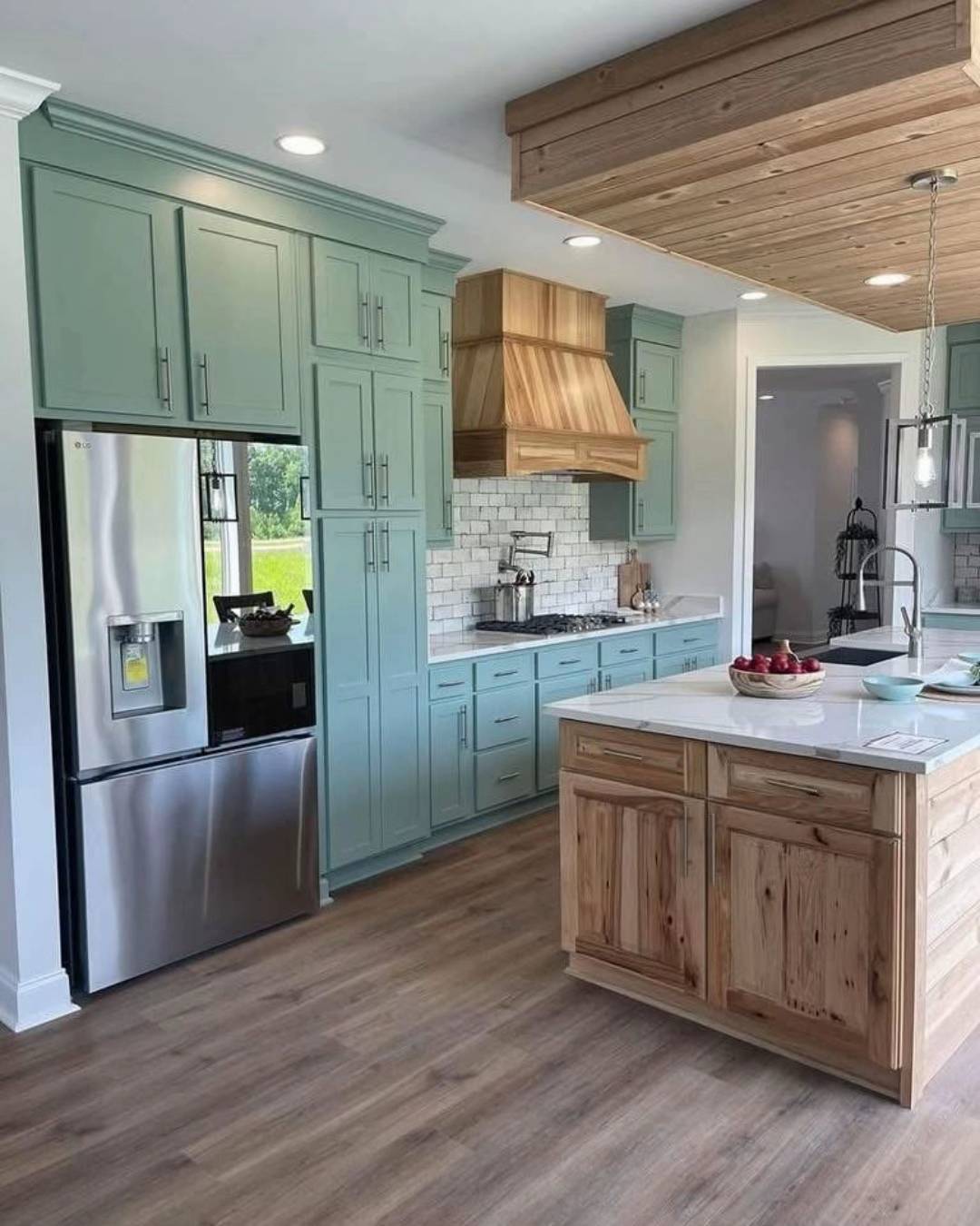 Modern kitchen with mint green cabinets, a stainless steel fridge, and a wooden island. Bright atmosphere with wood flooring and white backsplash.