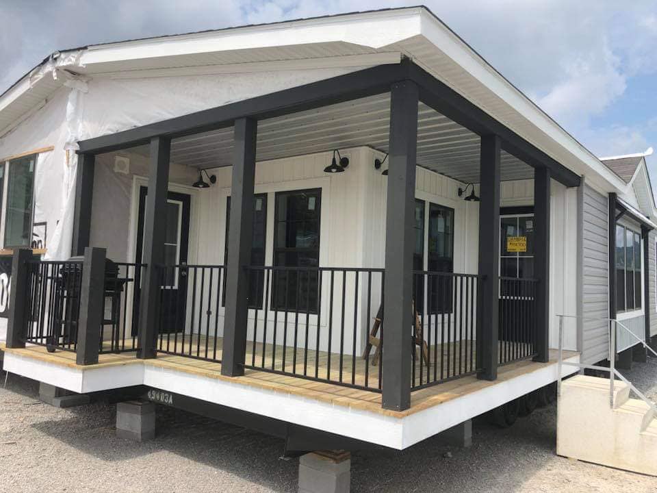 A modern modular home with a covered porch featuring black pillars and railings. The exterior has white siding, a black door, and large windows.