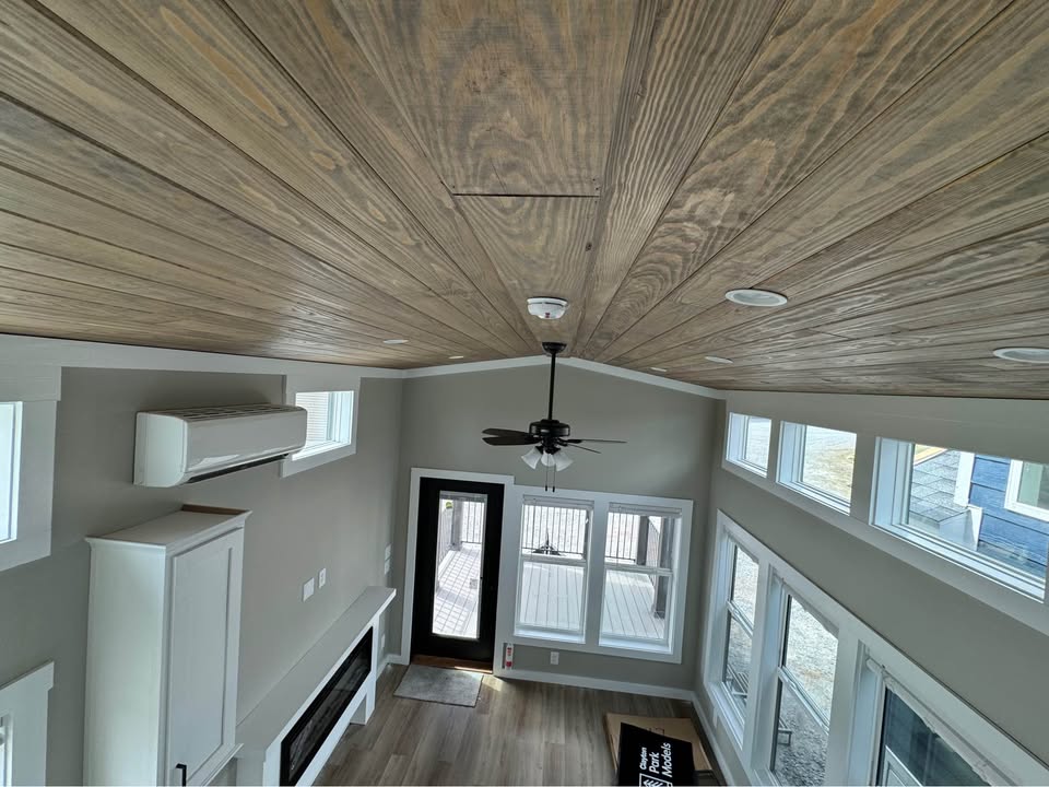 Stylish tiny home interior with wood-paneled ceiling, large windows, and ceiling fan. Bright, airy space emphasizes modernity and warmth.