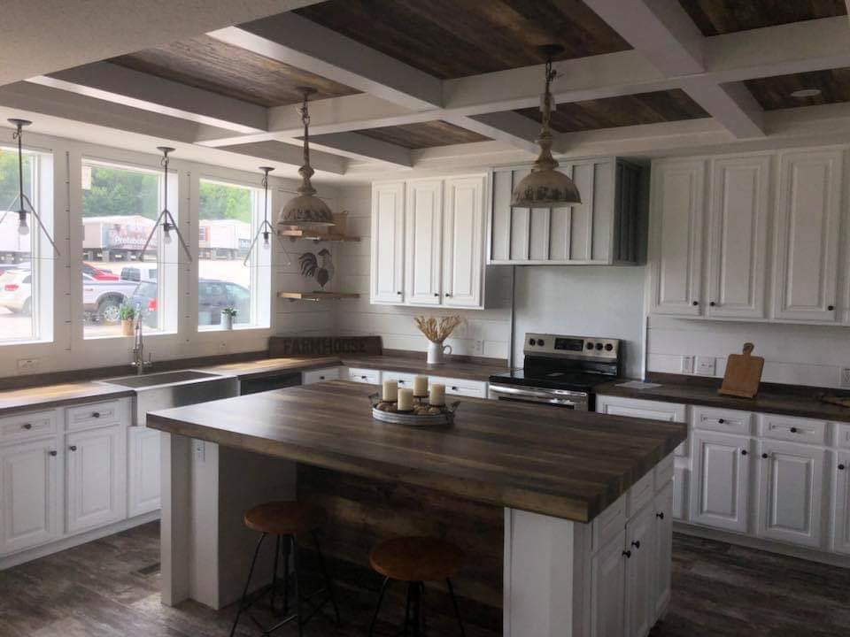 Spacious kitchen with white cabinets and a large wooden island. Rustic pendant lights, stainless steel appliances, and a farmhouse sign create a cozy atmosphere.
