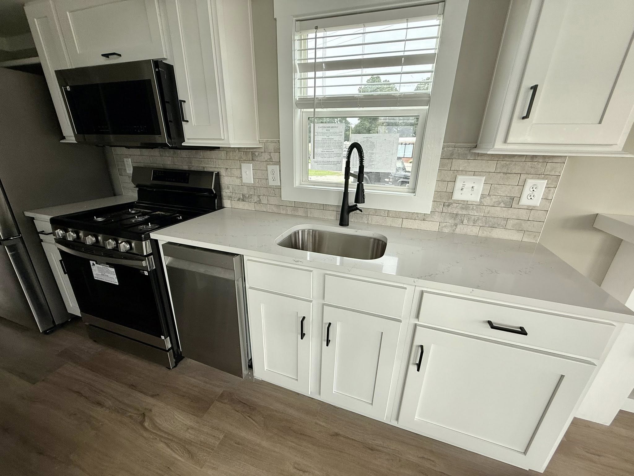 Modern kitchen with sleek white cabinets, stainless steel appliances, and a deep sink under a window. Light brick backsplash adds texture.