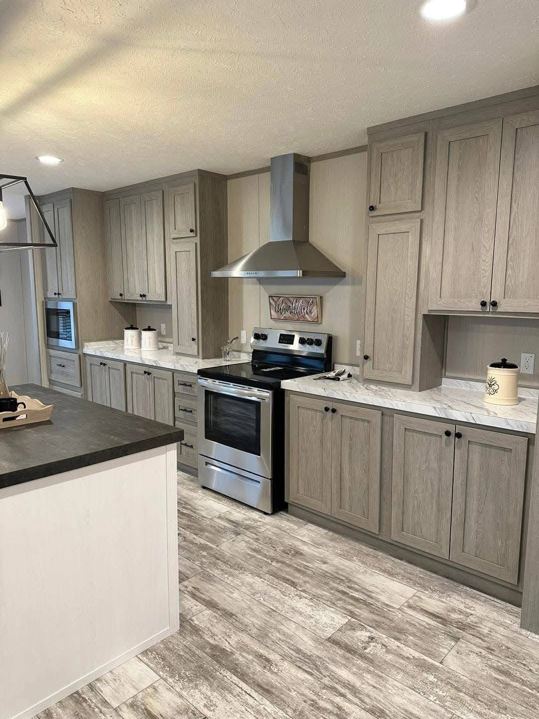 Modern kitchen with gray wood cabinets and a stainless steel stove. A marble countertop and light wood flooring create a warm, inviting atmosphere.