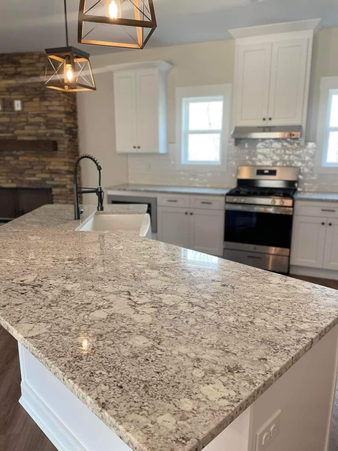 Modern kitchen with white cabinets and a large marble island. Stainless steel appliances, wood flooring, and a stone fireplace create a cozy ambiance.