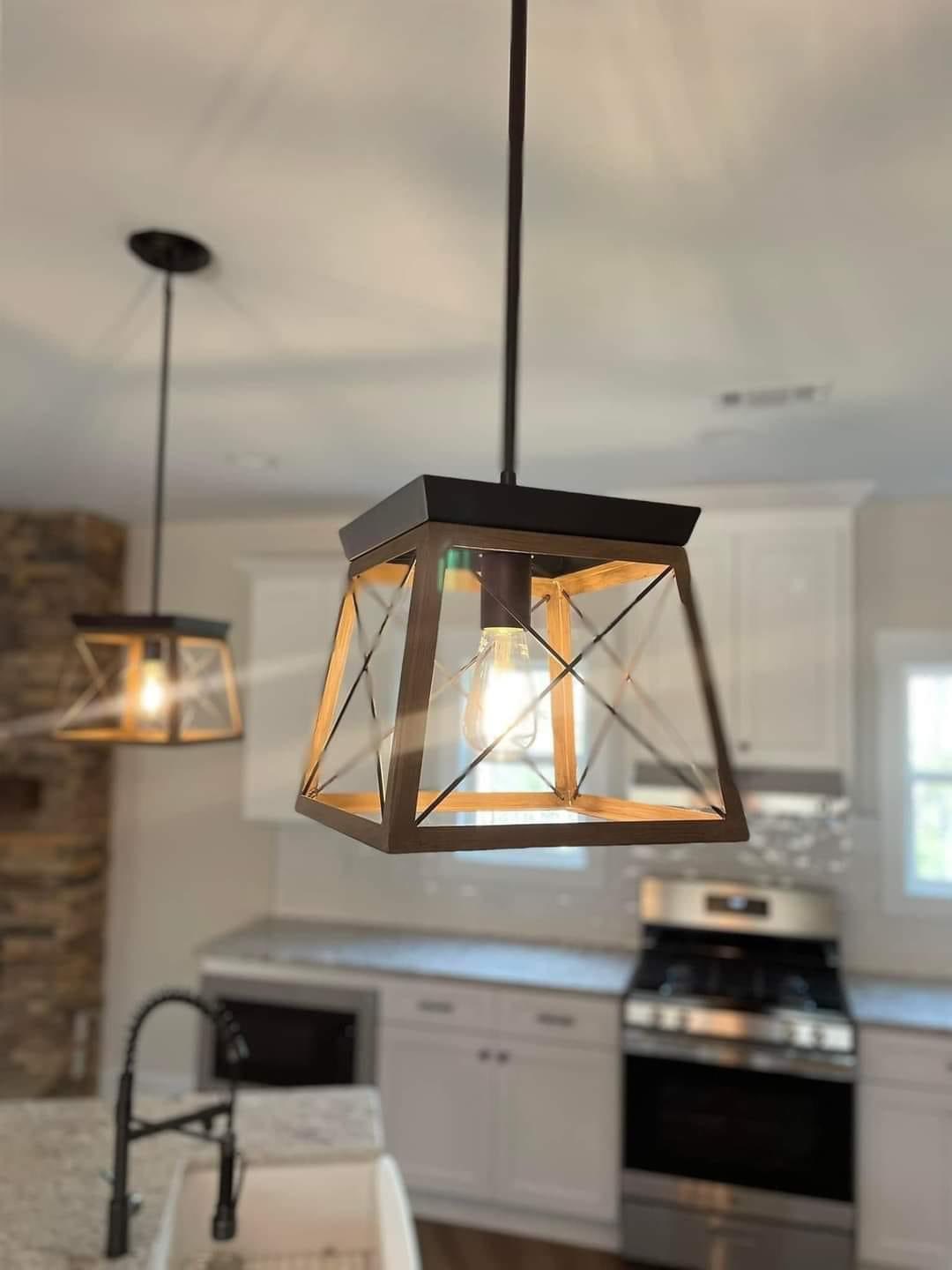 Modern kitchen interior featuring two geometric pendant lights with black frames, bright bulbs, granite countertops, and a stainless steel stove.