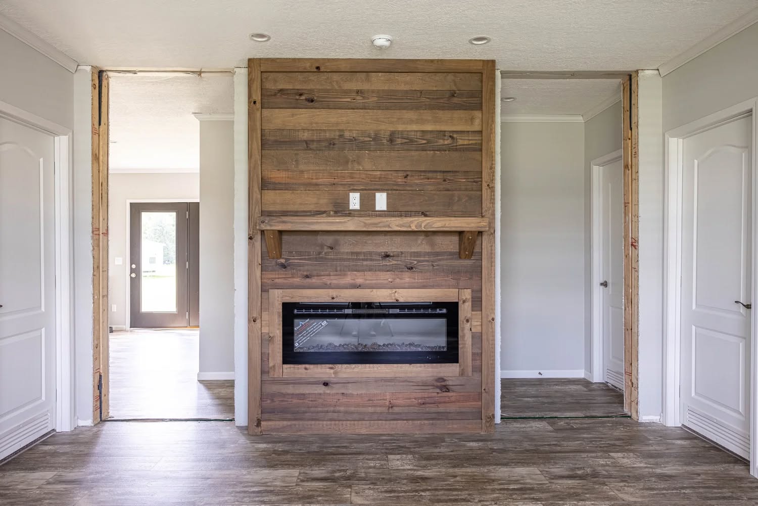 Modern living area featuring a rustic wooden accent wall with a built-in electric fireplace, flanked by white doors, creating a warm, inviting atmosphere.