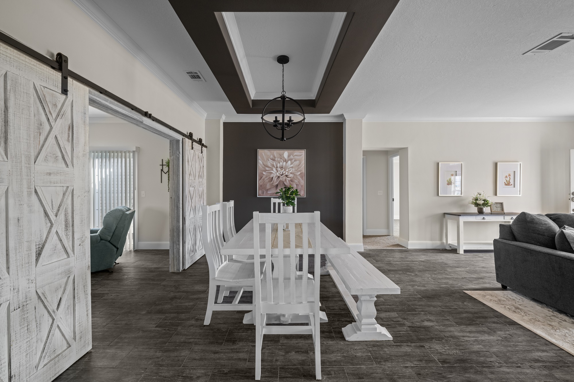 Spacious dining area with a white table and chairs, barn doors, dark accent wall, elegant lighting, and neutral decor creating a welcoming atmosphere.