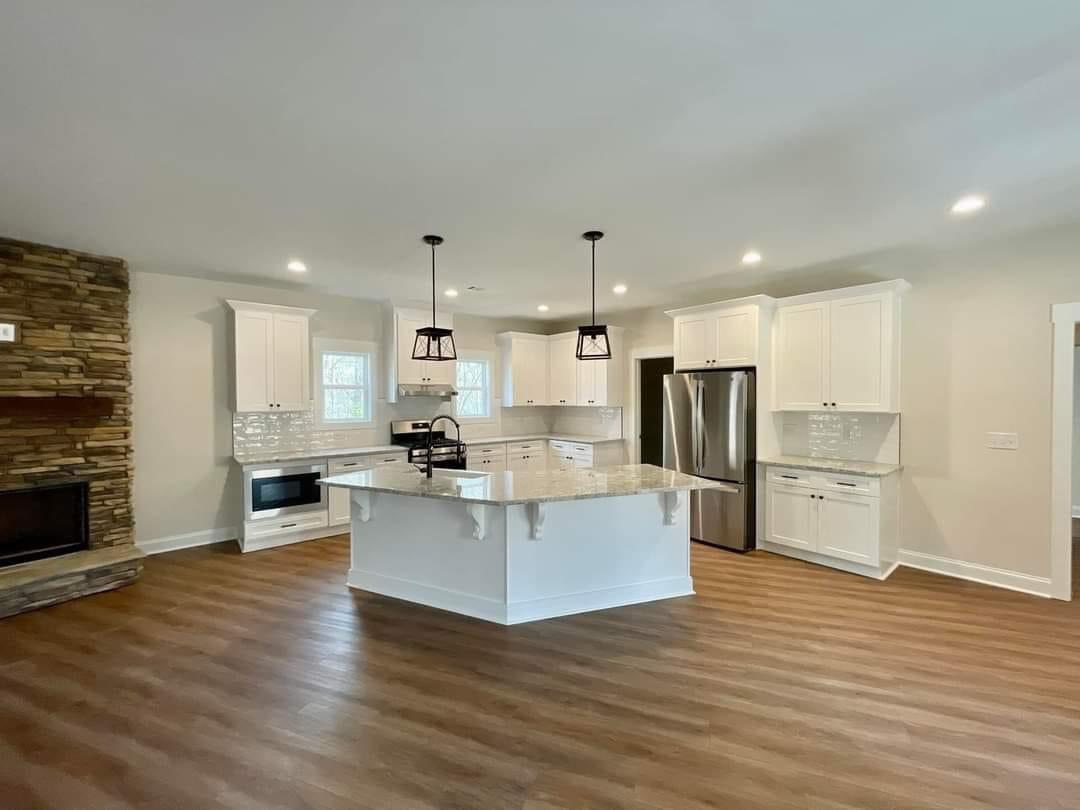 Modern kitchen with white cabinets and a large marble island. Stainless steel appliances, wood flooring, and a stone fireplace create a cozy ambiance.