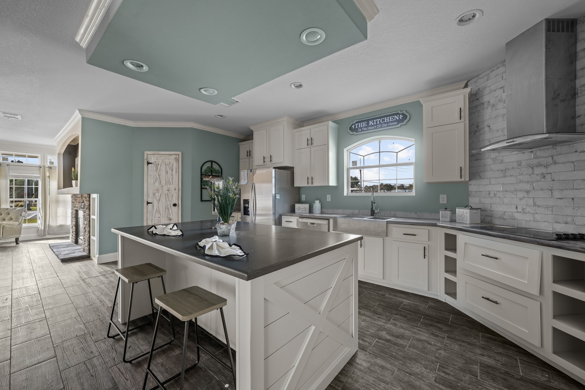 Spacious kitchen with a large island, gray countertops, and white cabinets. Light blue walls and brick backsplash create a modern, airy atmosphere.