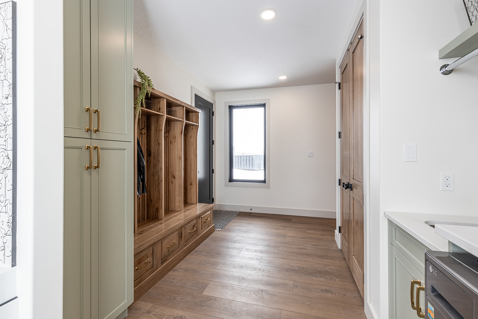 Modern mudroom with light wood flooring and a clean, minimalist design. Green cabinetry and wooden bench with coat hooks add warmth and functionality.