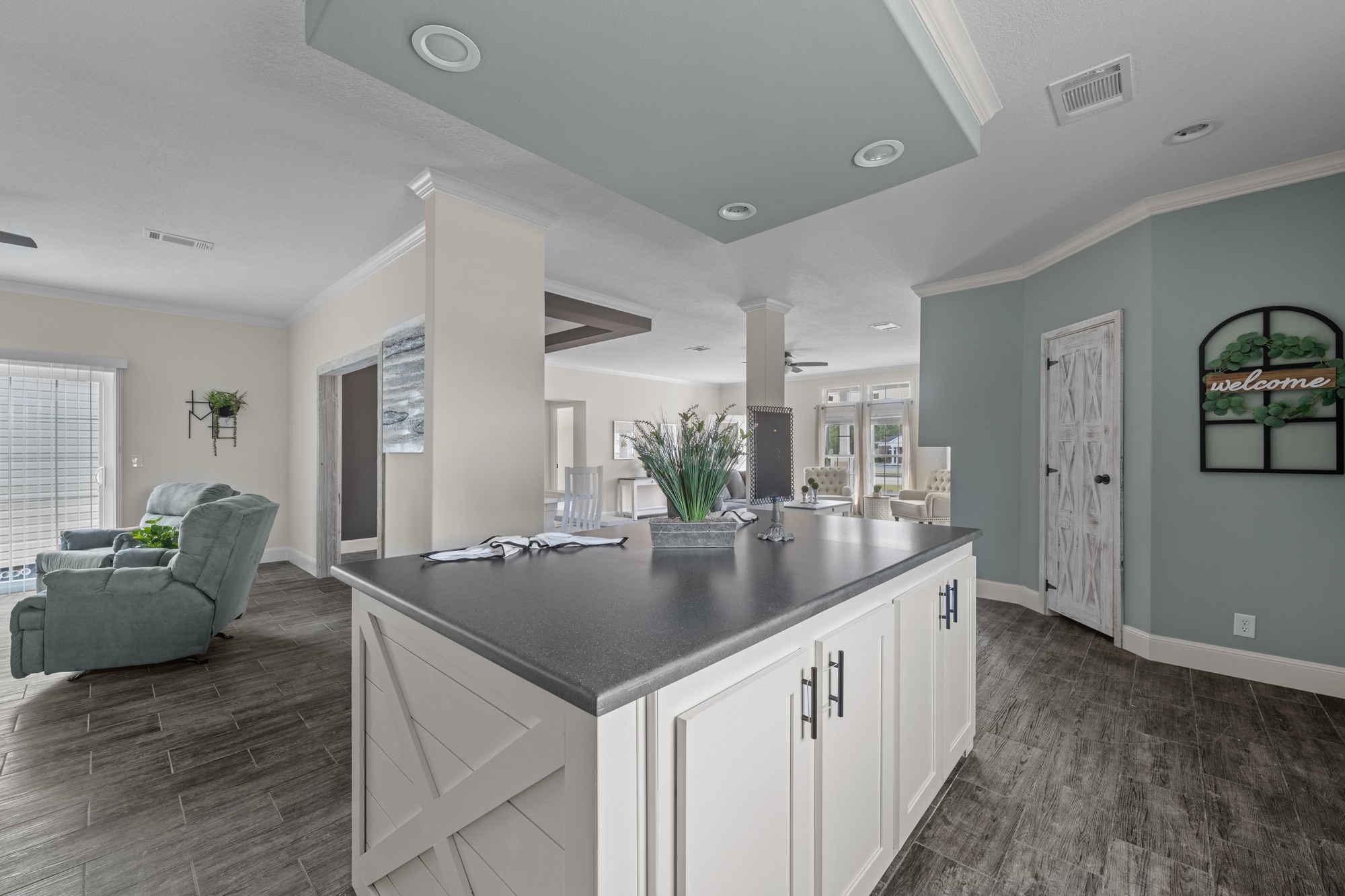 Modern open-concept living room with light green walls, hardwood floors, and a large kitchen island. Cozy armchairs and bright natural light enhance warmth.
