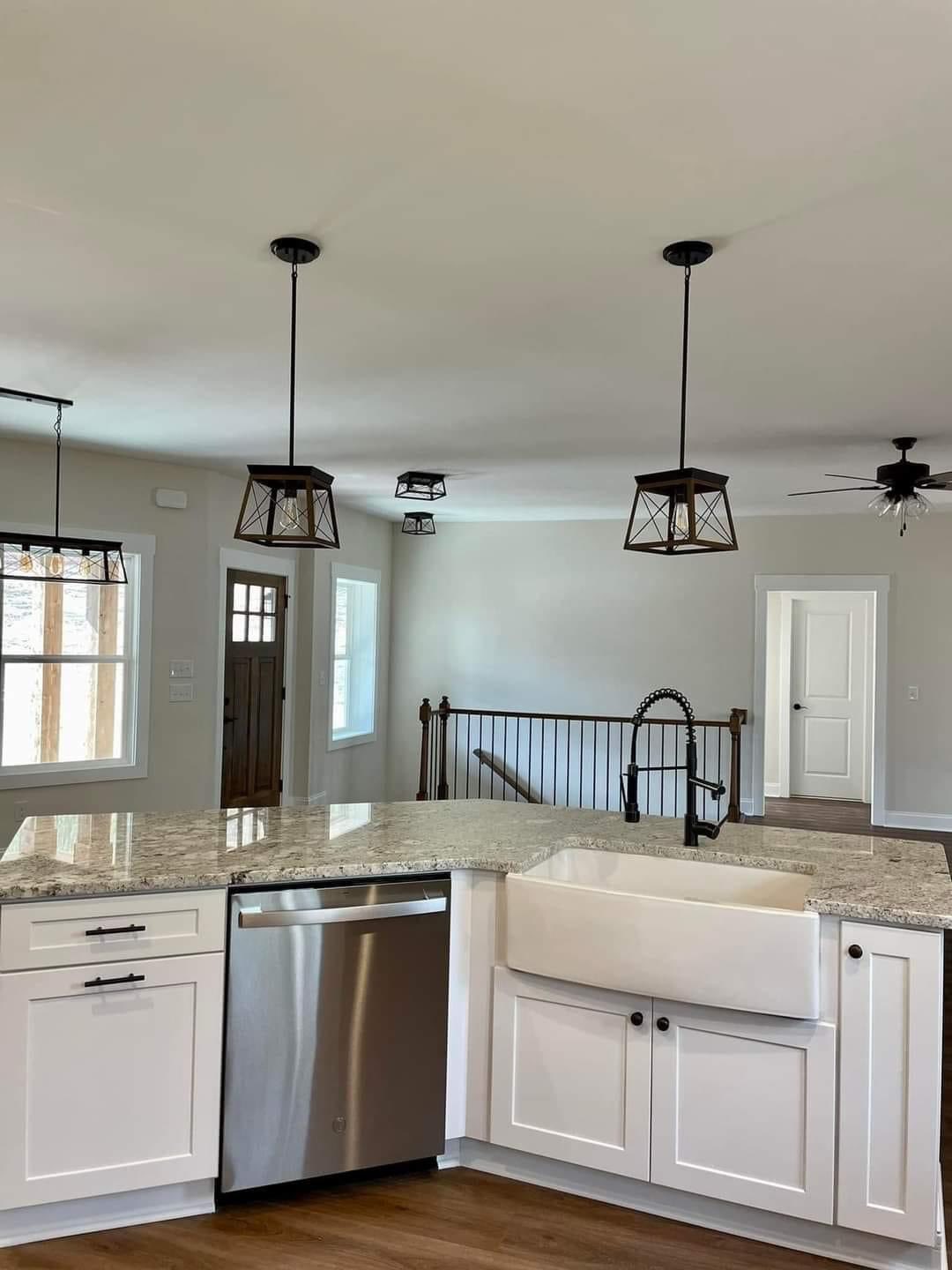 Bright modern kitchen with a large farmhouse sink, granite countertops, and pendant lights. Features include stainless steel appliances and wooden floors.