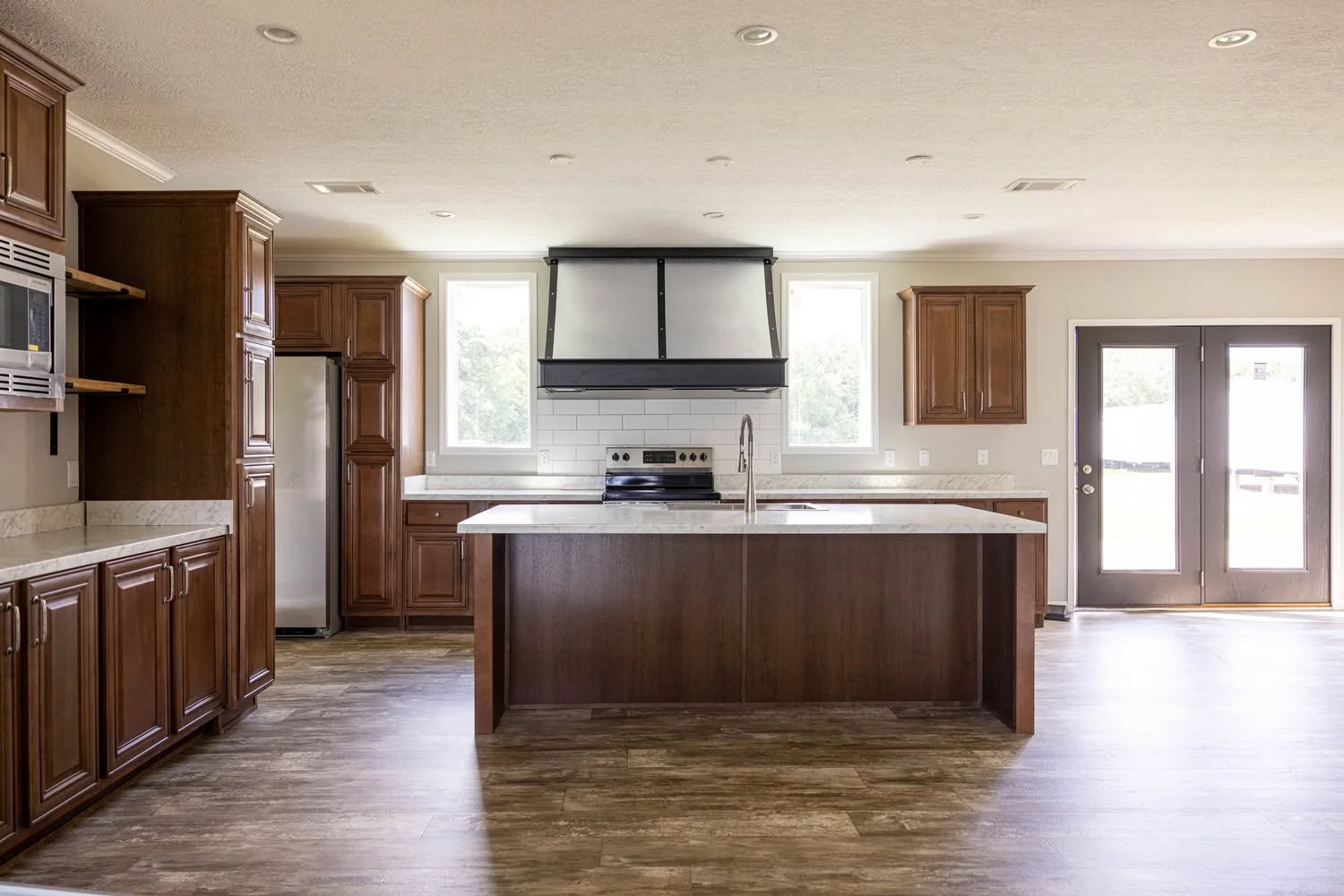 Spacious kitchen with a central island, dark wooden cabinets, stainless steel appliances, and large windows. Bright, modern, and minimalist style.