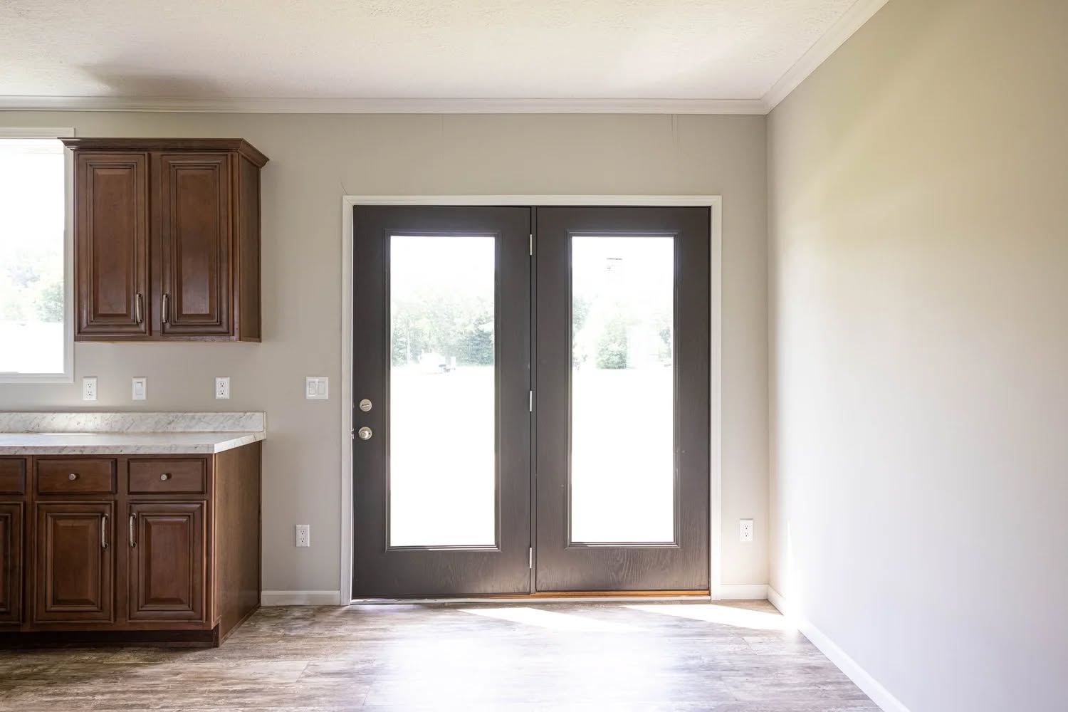 Bright room with wooden cabinets on the left, French doors with glass panes in the center, and light beige walls, creating a warm and inviting space.